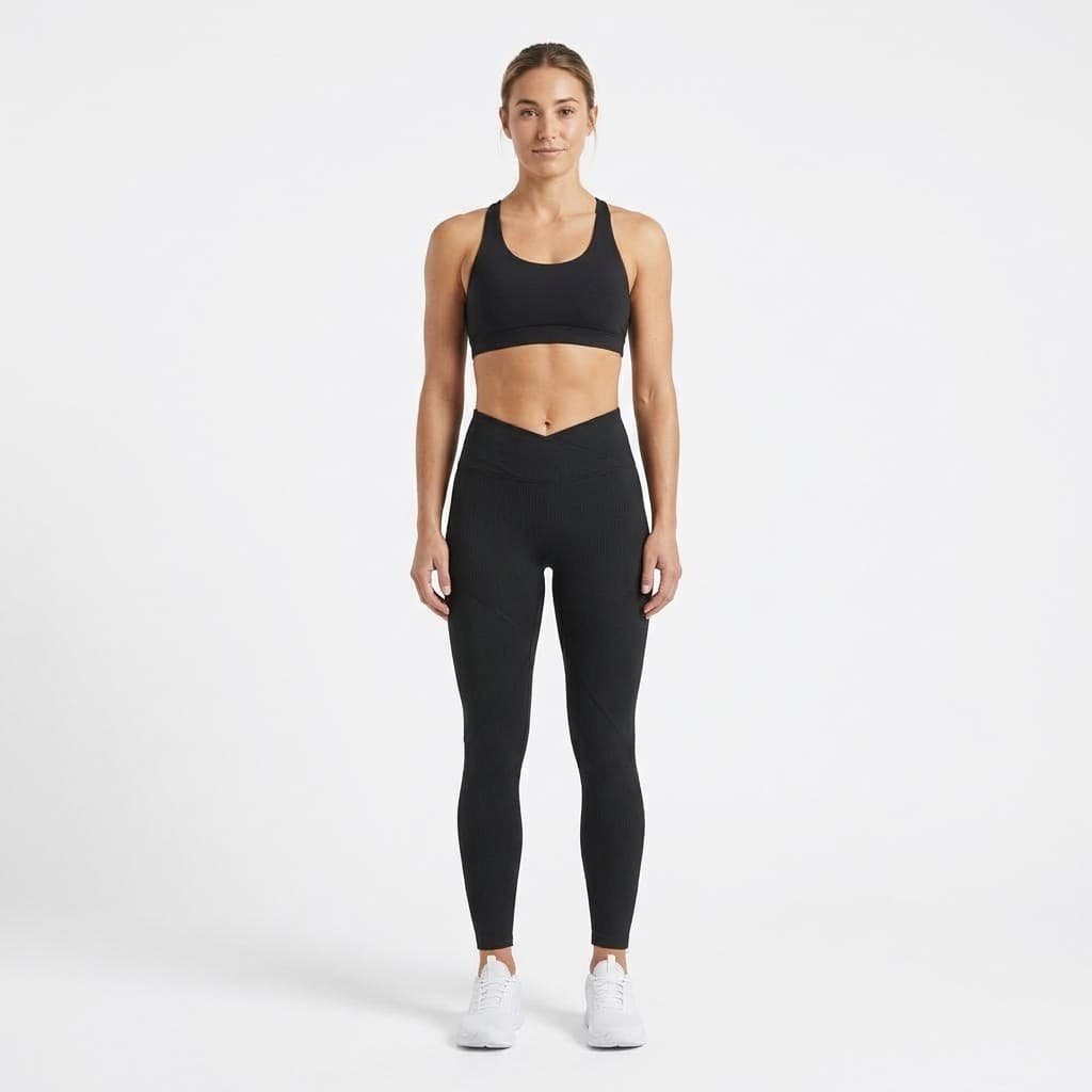 Fit woman standing straight in matte black crossover waist leggings with a black sports bra and white trainers