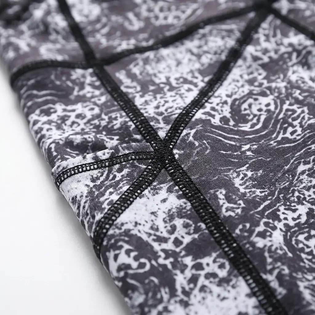 Close-up of the grey and white lace print on these pocket leggings, where black flat-lock seams cross by the pocket edge