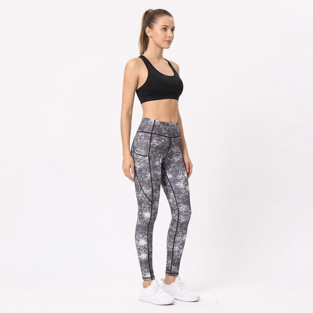 Fit woman turned slightly in dark lace print leggings with pockets, showing the side thigh pocket and black seam piping